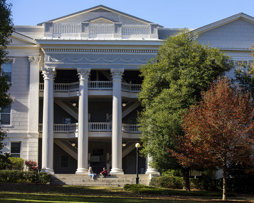 The front of the Holmes-Hunter Academic Building with students on the steps framed by North Campus trees turning red with colorful fall leaves.